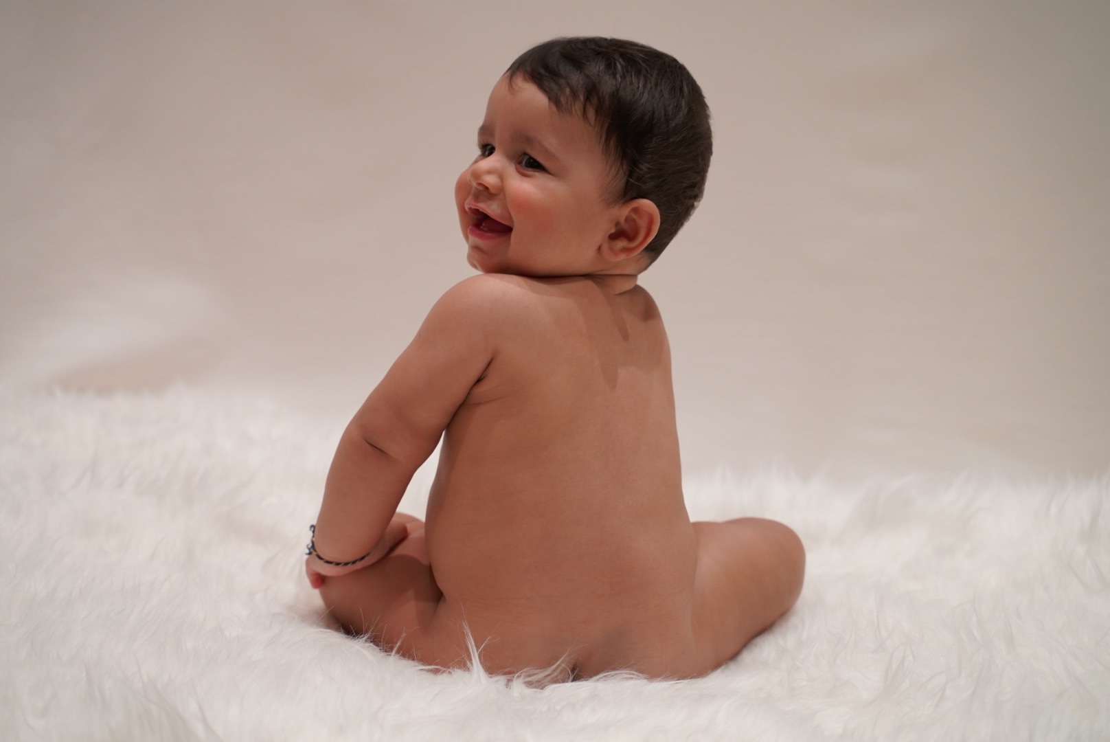 Baby smiling over their shoulder on a soft studio blanket