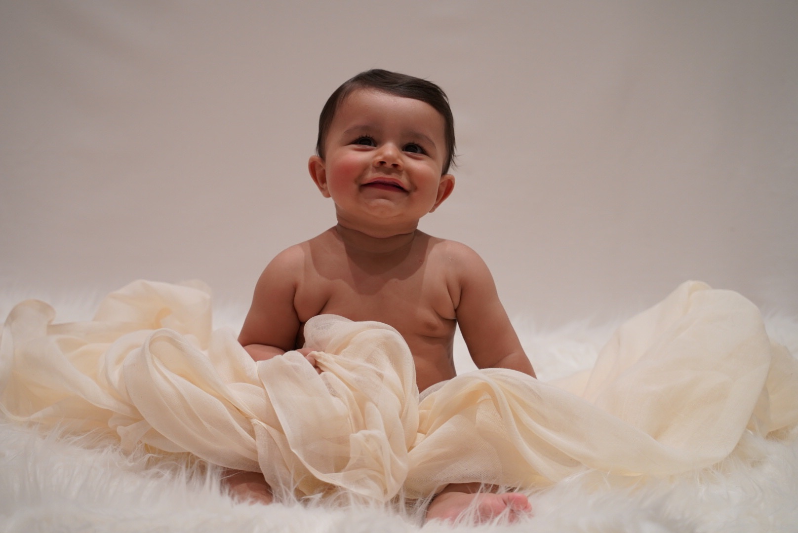 Baby smiling among soft cream fabric in the studio